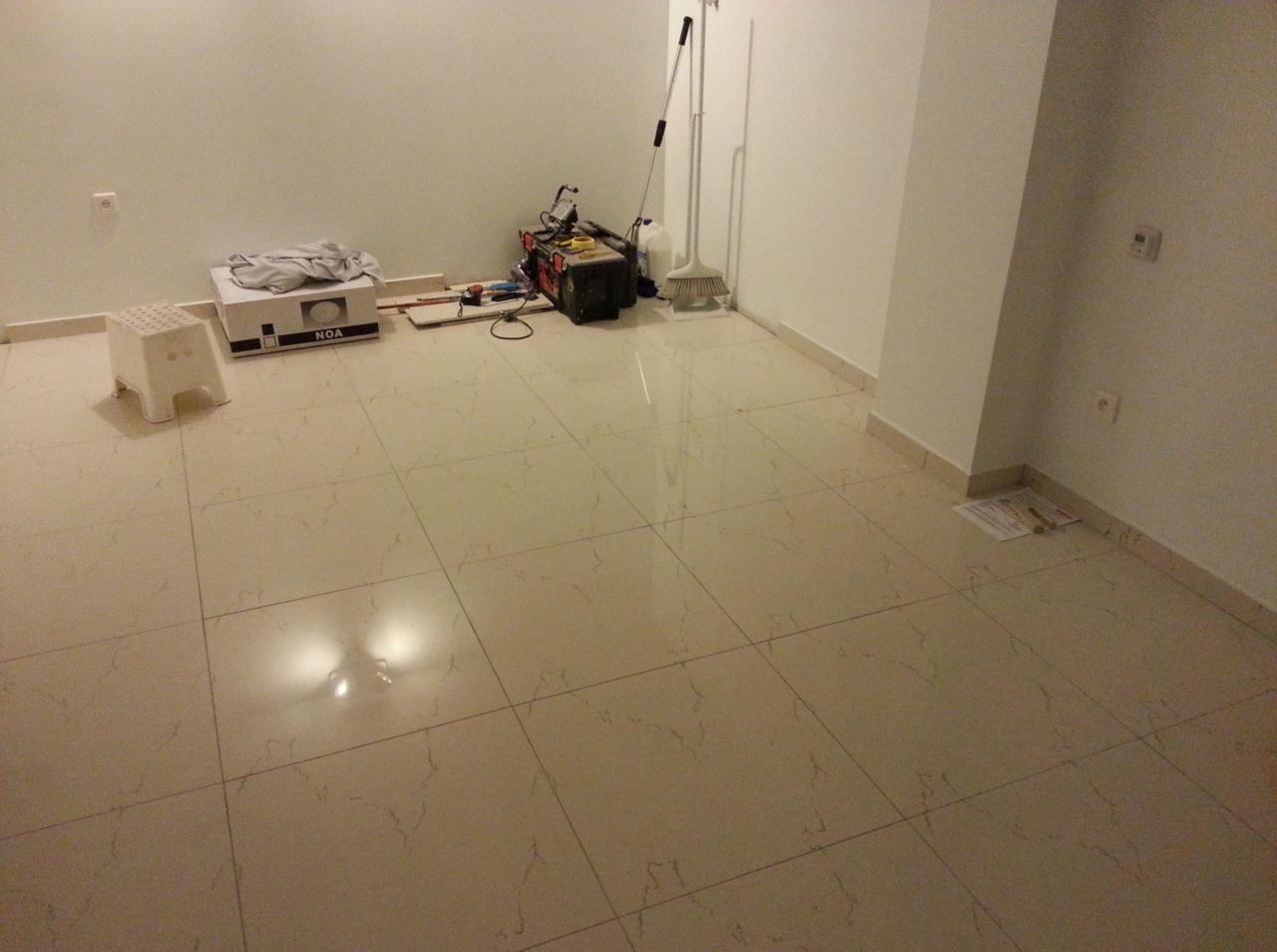 Przygotowania do montażu: białe płytki podłogowe w nowym pomieszczeniu, karton NOA, narzędzia, drabinka i zmiotka przy ścianie.