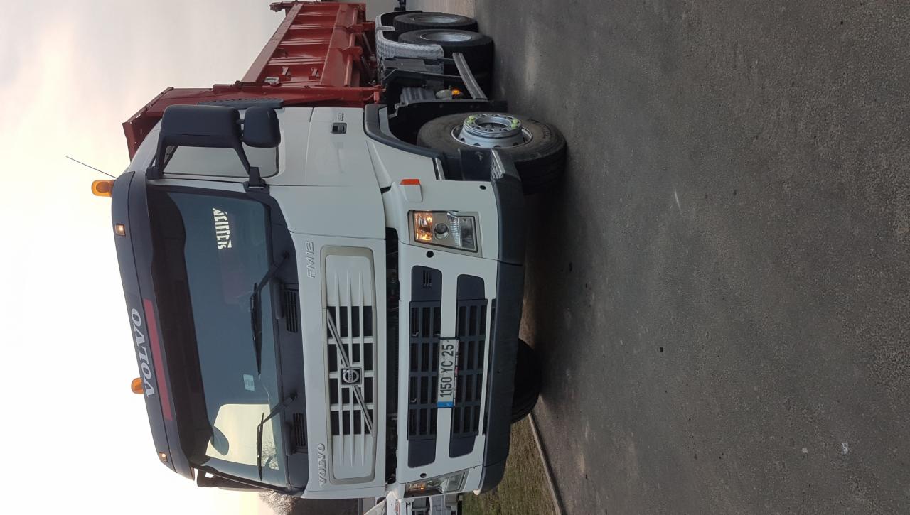 Ciężarówka Volvo FMX z czerwoną skrzynią ładunkową, zaparkowana na asfaltowej powierzchni, widoczna z przodu i boku, z pomarańczowym światłem ostrzegawczym na dachu.