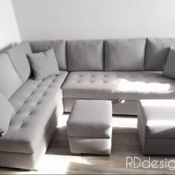 Jasnoszara, narożna sofa z pikowanymi siedziskami i dwoma pufami w minimalistycznym wnętrzu, oświetlona naturalnym światłem.