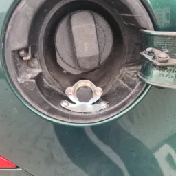 Zielony samochód: zbliżenie na wlew paliwa z zamontowanym metalowym zabezpieczeniem na korek wlewu.