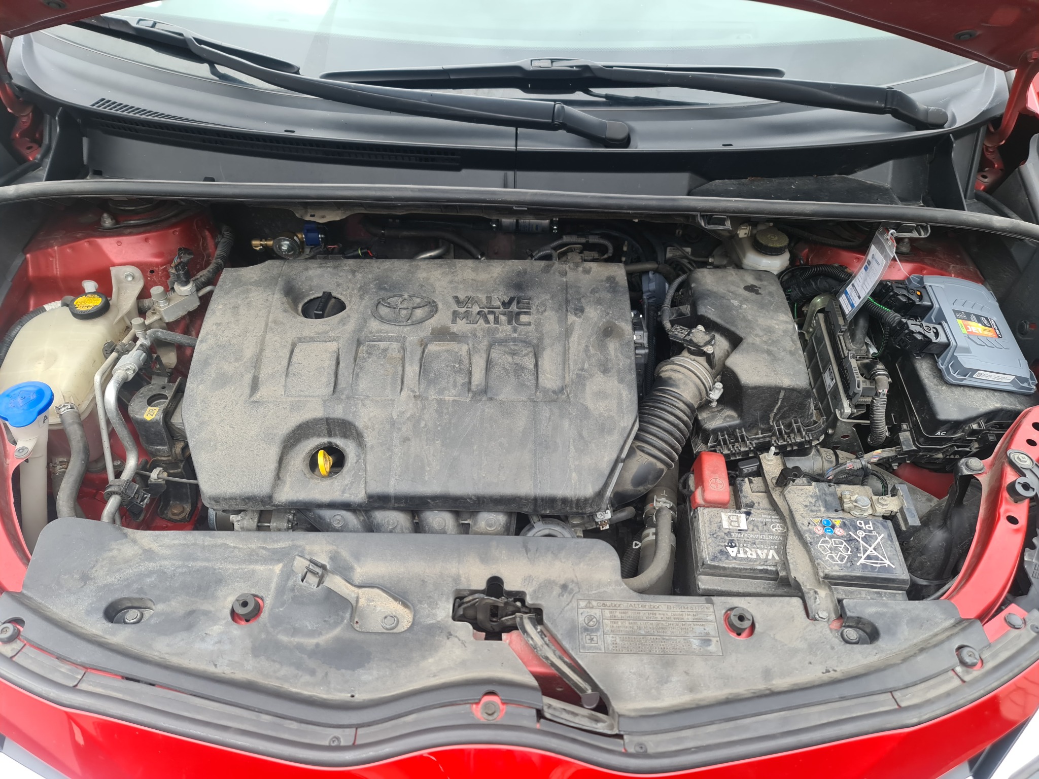 Otwarta maska czerwonego samochodu z widocznym silnikiem Valvematic, akumulatorem Varta i instalacją LPG z nowym sterownikiem Jet.