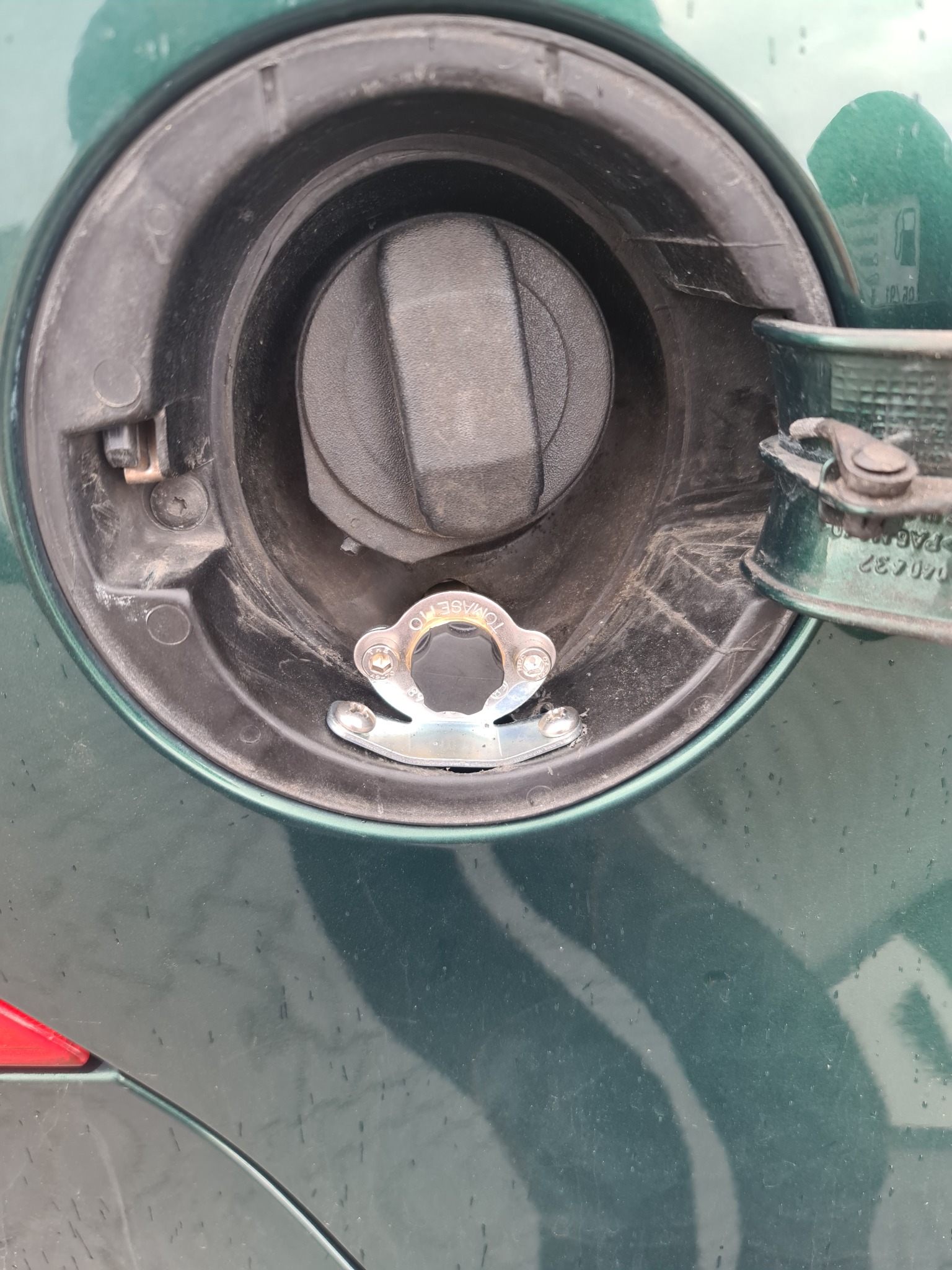 Zielony samochód: zbliżenie na wlew paliwa z zamontowanym metalowym zabezpieczeniem na korek wlewu.