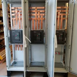 Otwarty rozdzielnica elektryczna z miedzianymi szynami zbiorczymi i wyłącznikami, widoczne elementy montażowe i konstrukcja wewnętrzna.