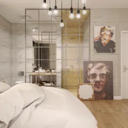 Nowoczesna sypialnia z łazienką oddzieloną szklaną ścianą w metalowej ramie, wiszące żarówki Edison, betonowe ściany i podłoga z paneli, obrazy na ścianie, biała pościel na łóżku.
