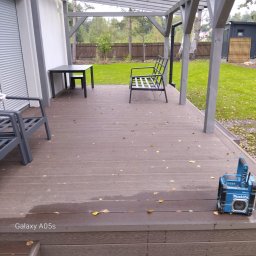 TRANSBUD BLOCH SPÓŁKA Z OGRANICZONĄ ODPOWIEDZIALNOŚCIĄ - Nowoczesny taras z kompozytowych desek w odcieniach brązu, z szarymi meblami ogrodowymi i radiem budowlanym Makita. Widoczne jesienne liście na powierzchni.