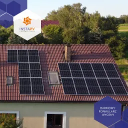 Instalacja paneli słonecznych na dachu domu z czerwoną dachówką, widoczne okno dachowe i komin, w tle zieleń drzew i budynek, w rogu logo firmy i napis 'Darmowy formularz wyceny'.