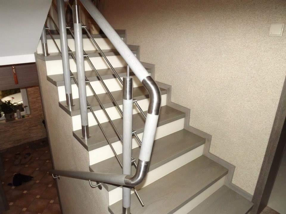 Schody wewnętrzne z szarymi stopniami i białą podstopnicą, balustrada ze stali nierdzewnej z elementami drewnianymi, widok z dołu na górę.