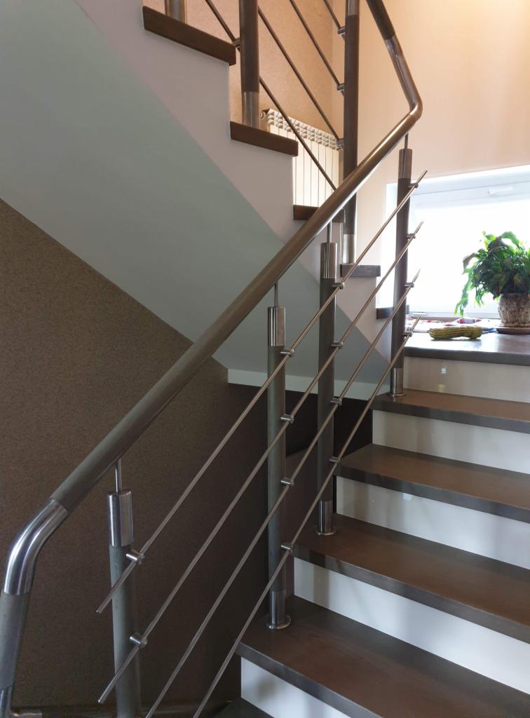 Schody z drewnianymi stopniami i metalową balustradą z rurek, widok z dołu, na podeście doniczka z zieloną rośliną.