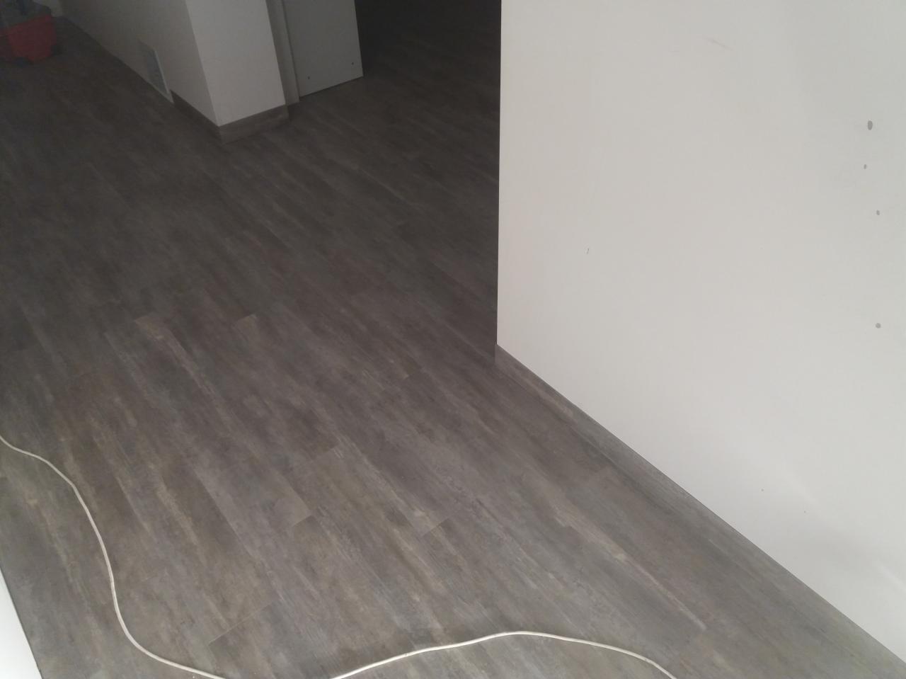 Ułożona, szara wykładzina imitująca drewno w korytarzu, widoczny kabel przy podłodze.