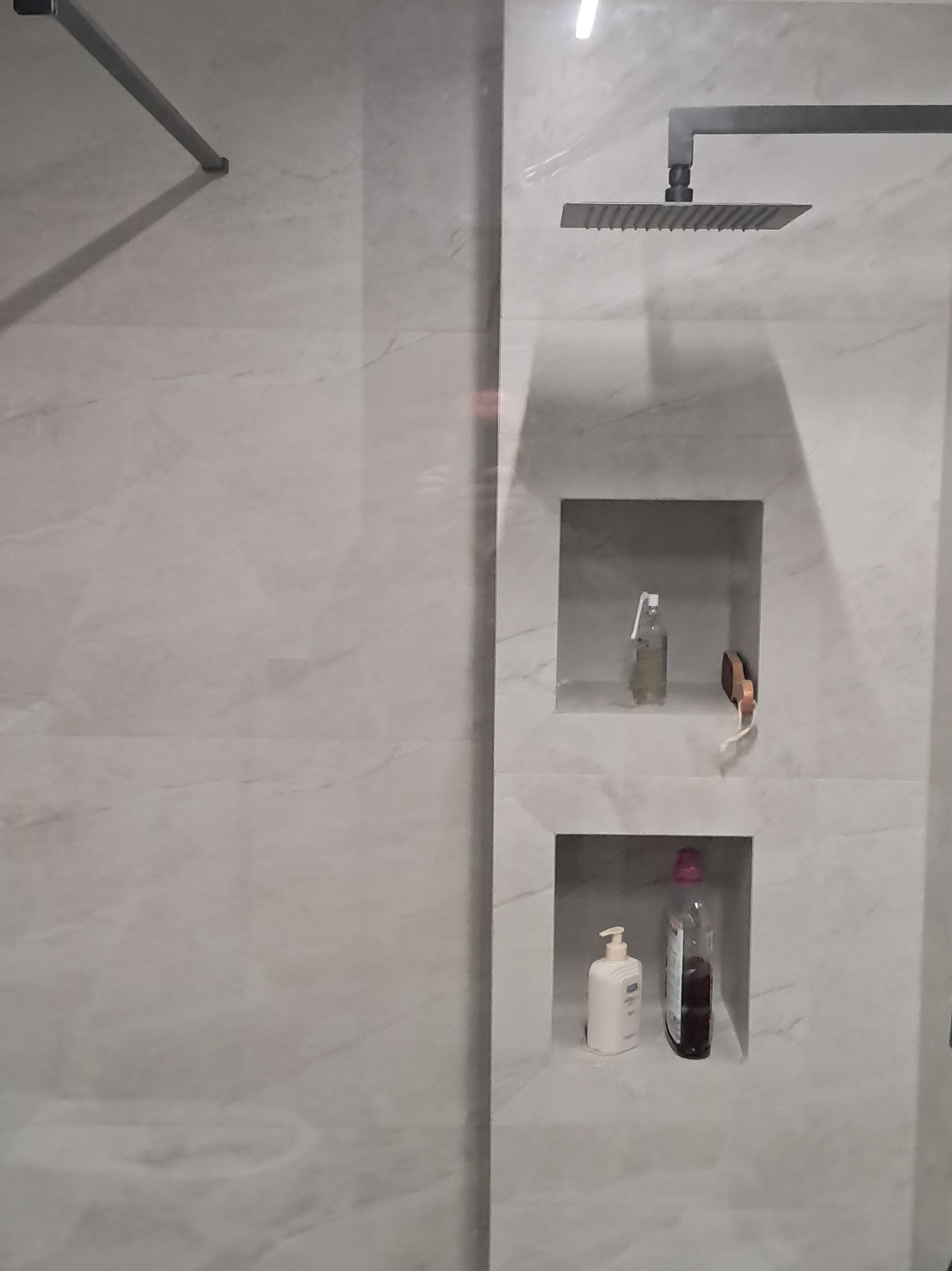 Wykończona kabina prysznicowa z szarymi płytkami imitującymi marmur, z wnękami na kosmetyki i deszczownicą