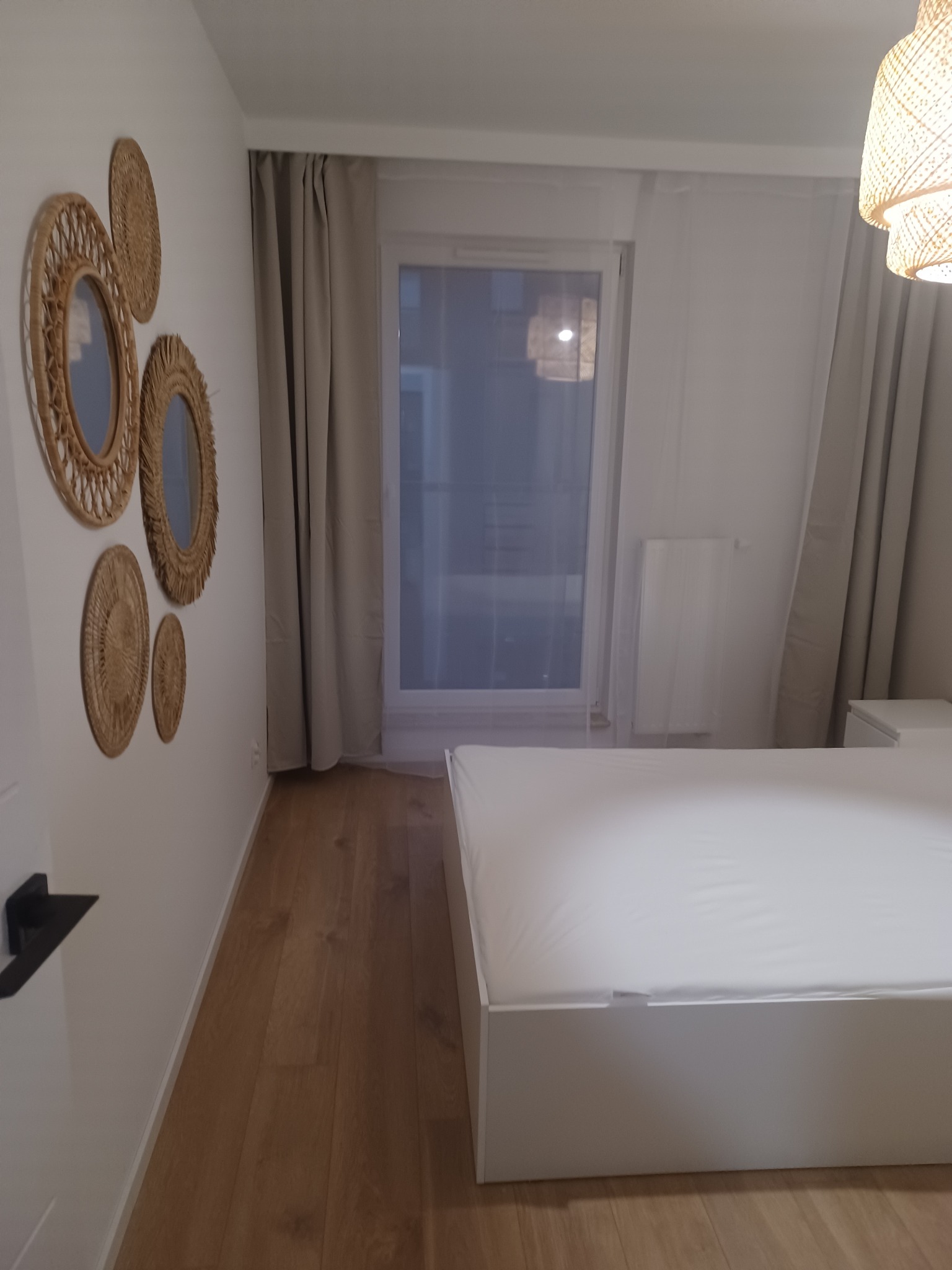 Jasna sypialnia z białym łóżkiem, drewnianą podłogą i dekoracyjnymi lustrami z rafii na ścianie