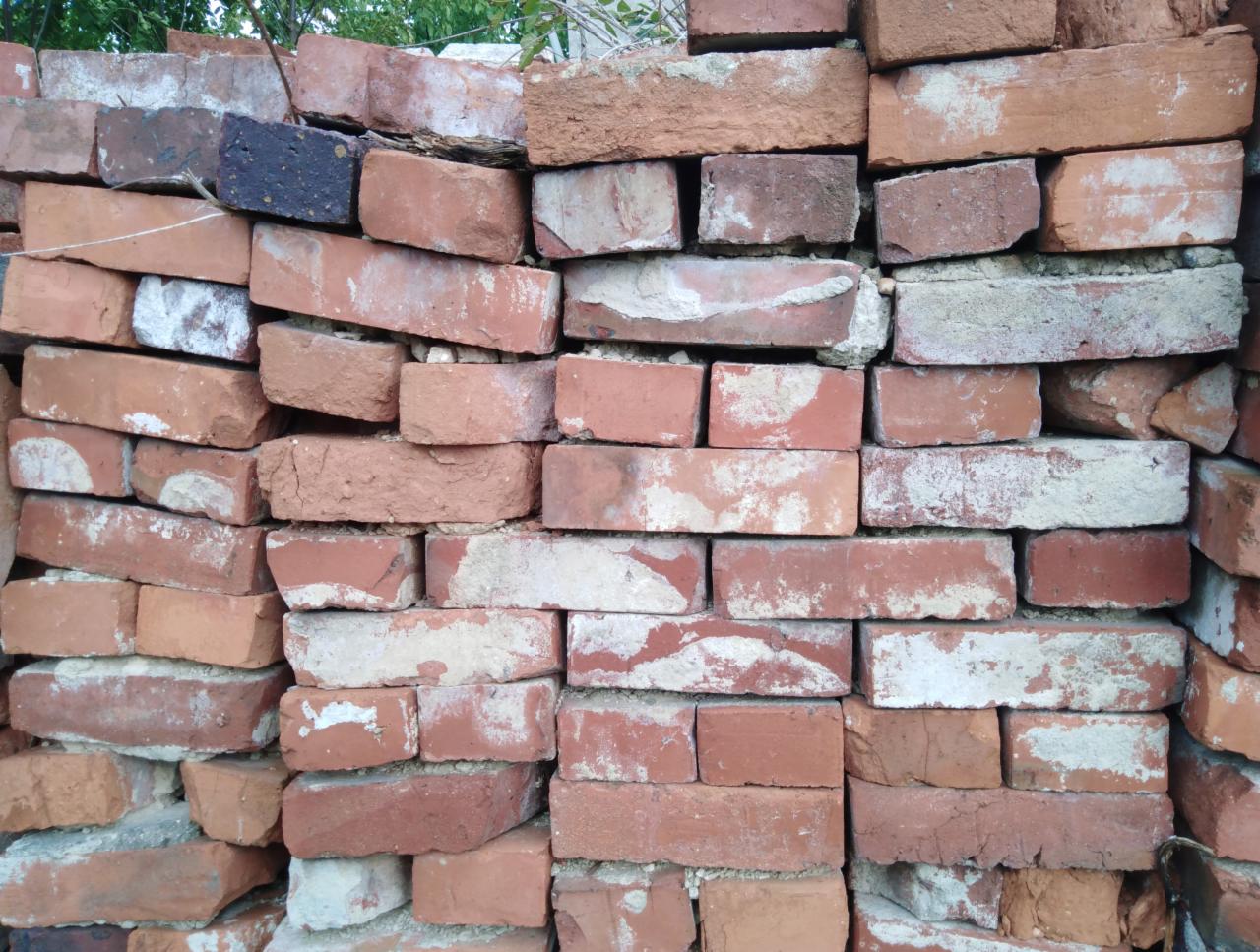 Stos czerwonych, używanych cegieł z resztkami zaprawy, ułożonych nieregularnie na zewnątrz.