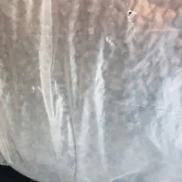 Przezroczysty worek foliowy wypełniony drobnymi, ciemnymi przedmiotami, prawdopodobnie gruzem lub odpadami budowlanymi.