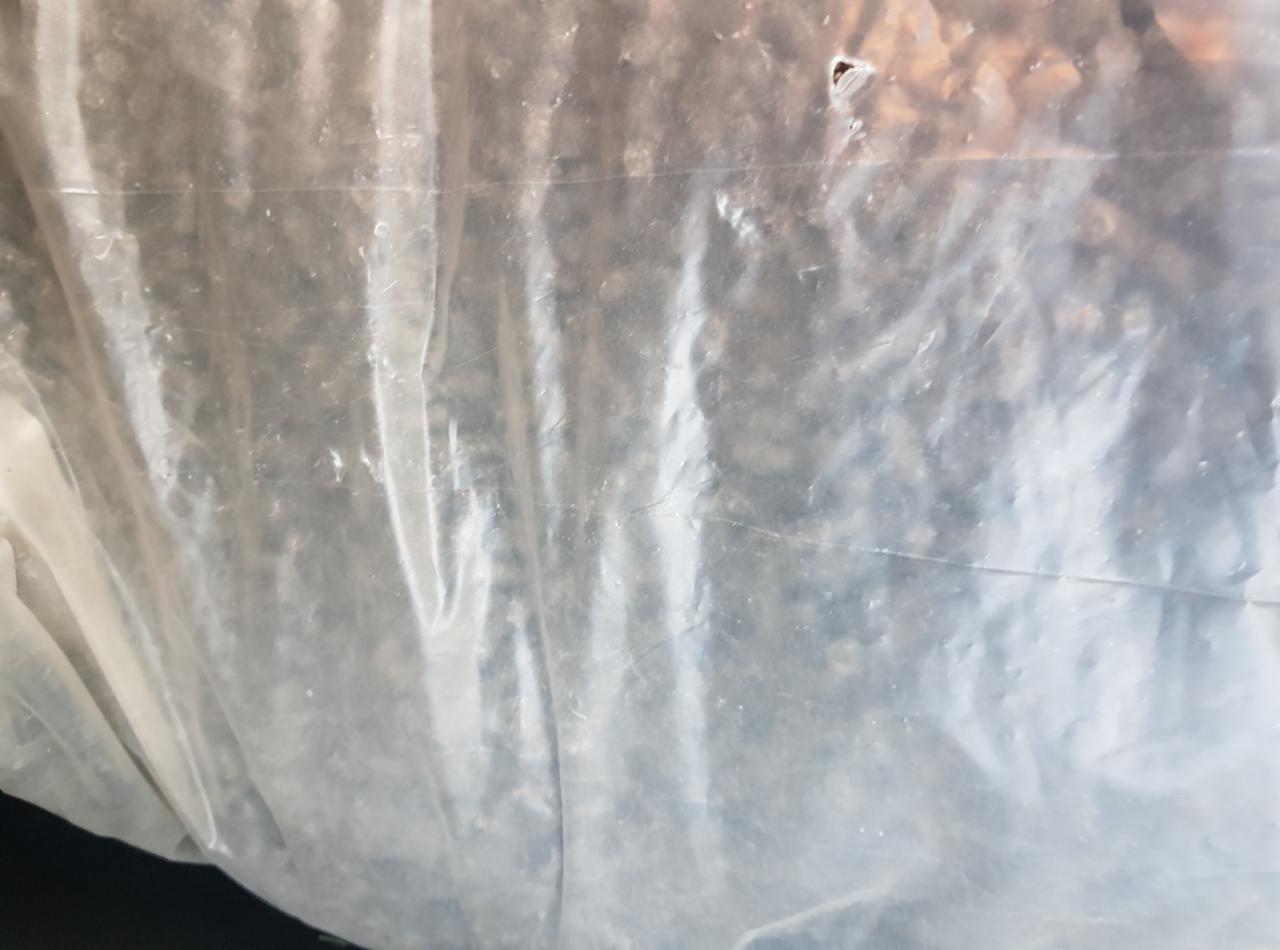 Przezroczysty worek foliowy wypełniony drobnymi, ciemnymi przedmiotami, prawdopodobnie gruzem lub odpadami budowlanymi.