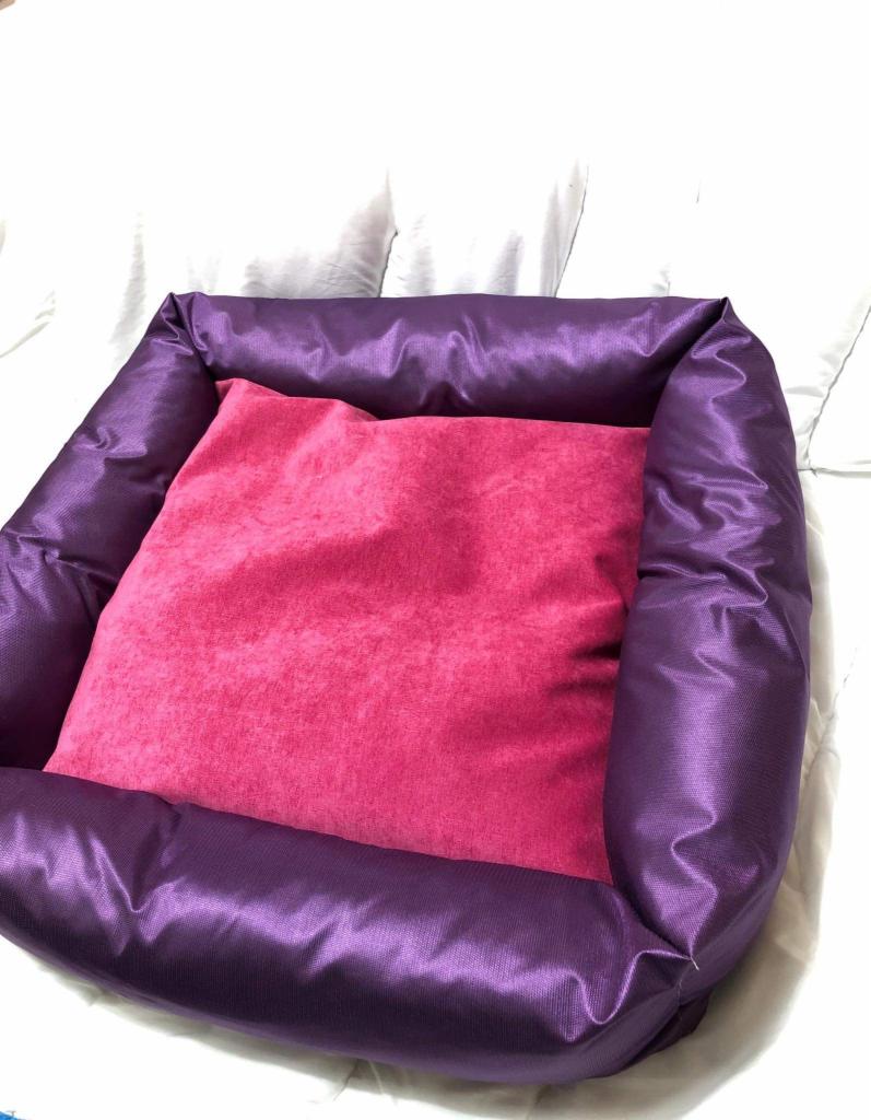 Fioletowe legowisko dla psa z różową poduszką w środku, leżące na białej pościeli.