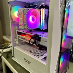 Wnętrze białej obudowy komputera stacjonarnego z podświetleniem RGB, widoczne wentylatory, karta graficzna Radeon i pamięć RAM, całość na stole.