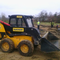 HGO Sp. z o.o. - Żółto-czarna miniładowarka JCB na placu budowy, w tle pracownicy w kamizelkach odblaskowych. Sprzęt firmy Ramirent.