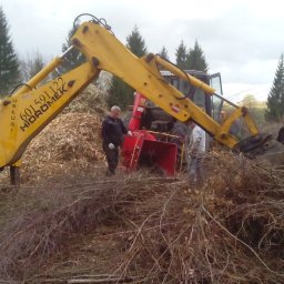 HGO Sp. z o.o. - Żółta koparka z podnośnikiem i rozdrabniaczem gałęzi w akcji. Pracownicy obsługują maszynę, a w tle widać drzewa i zrębki.
