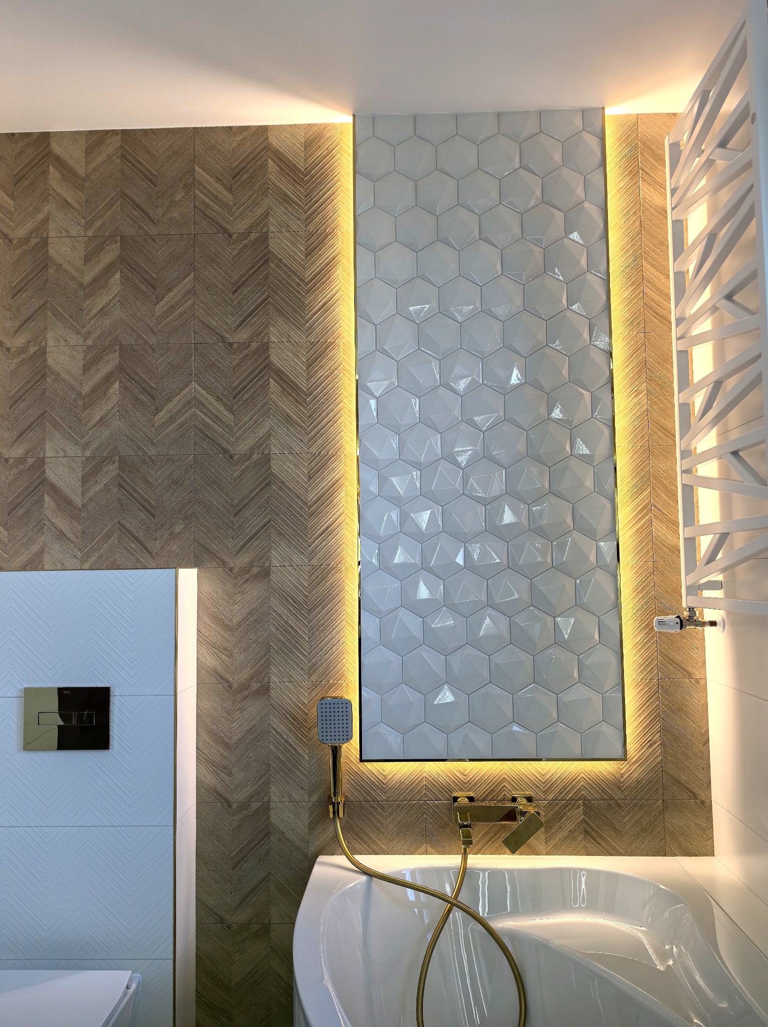 Nowoczesna łazienka z wanną, mozaiką heksagonalną podświetloną LED i drewnopodobnymi płytkami ułożonymi w jodełkę. Złota armatura i grzejnik drabinkowy.