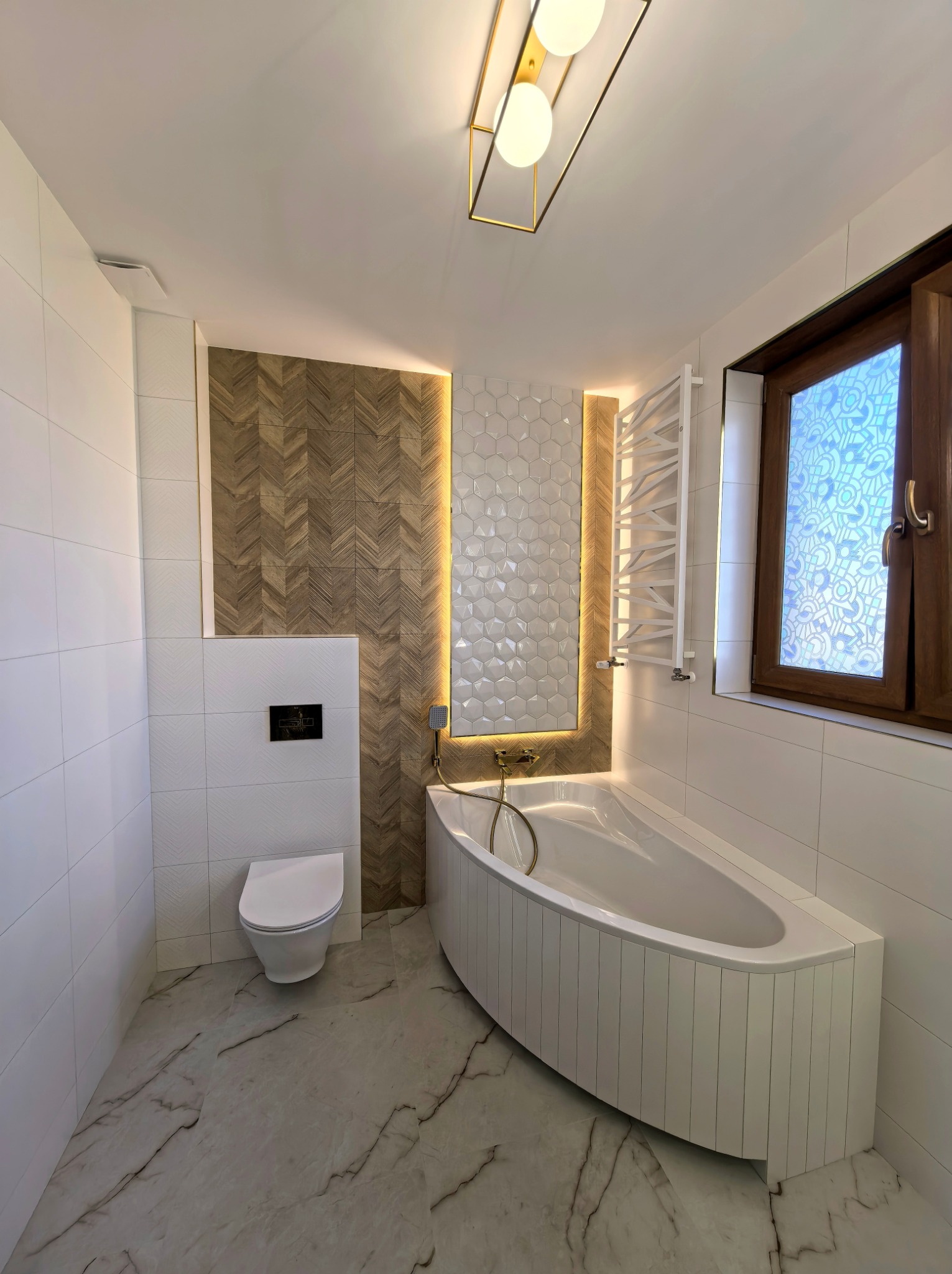 Nowoczesna łazienka z wanną narożną obudowaną panelami, mozaiką heksagonalną z podświetleniem LED i płytkami imitującymi drewno ułożonymi w jodełkę.