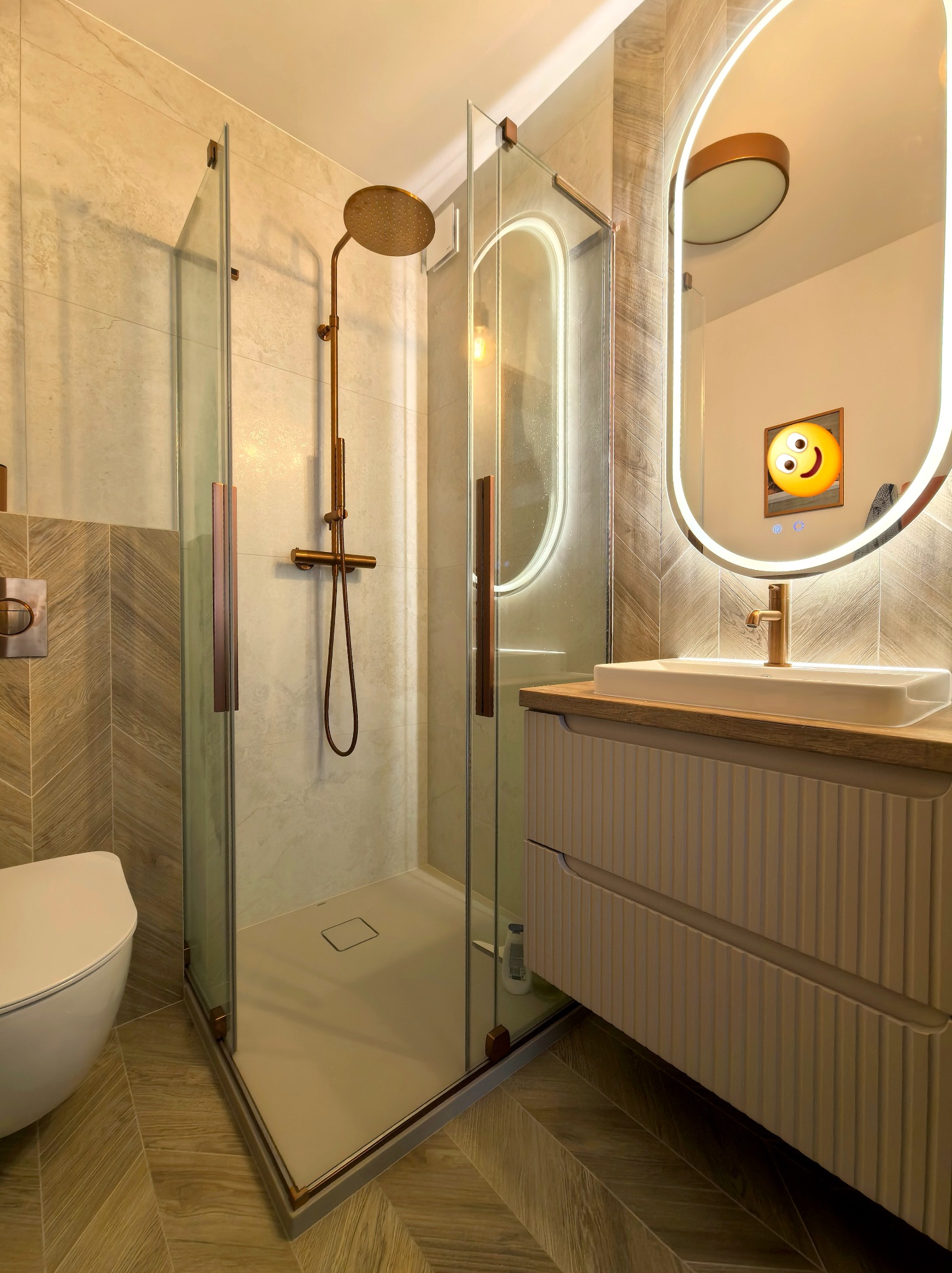 Nowoczesna łazienka z kabiną prysznicową typu walk-in, umywalką na szafce z frezowanymi frontami i podświetlanym lustrem. Uwagę zwracają złote detale armatury.