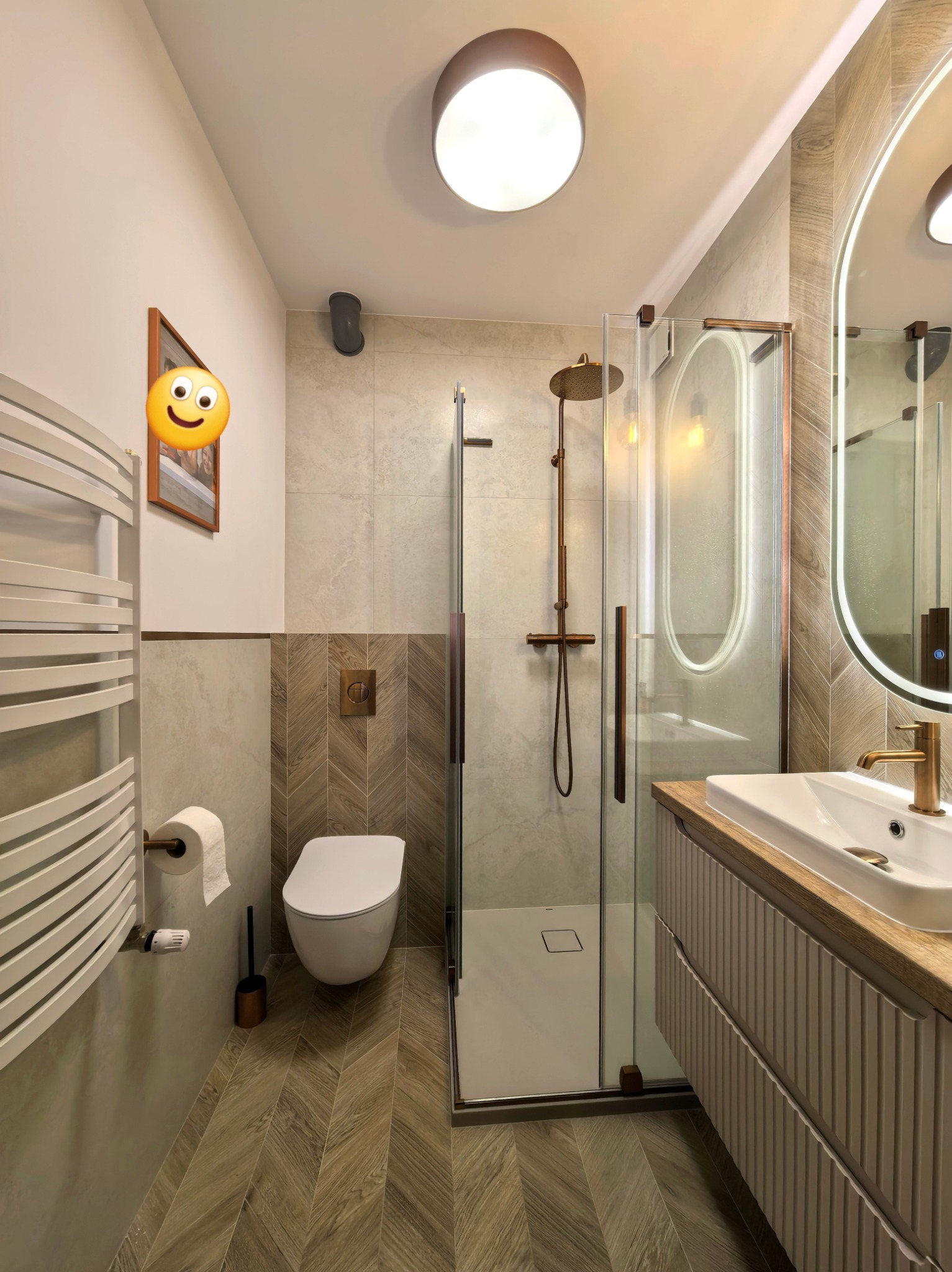 Nowoczesna łazienka z kabiną prysznicową typu walk-in, umywalką na szafce z drewnianym blatem i grzejnikiem drabinkowym. Uwagę zwracają płytki ułożone w jodełkę na podłodze.