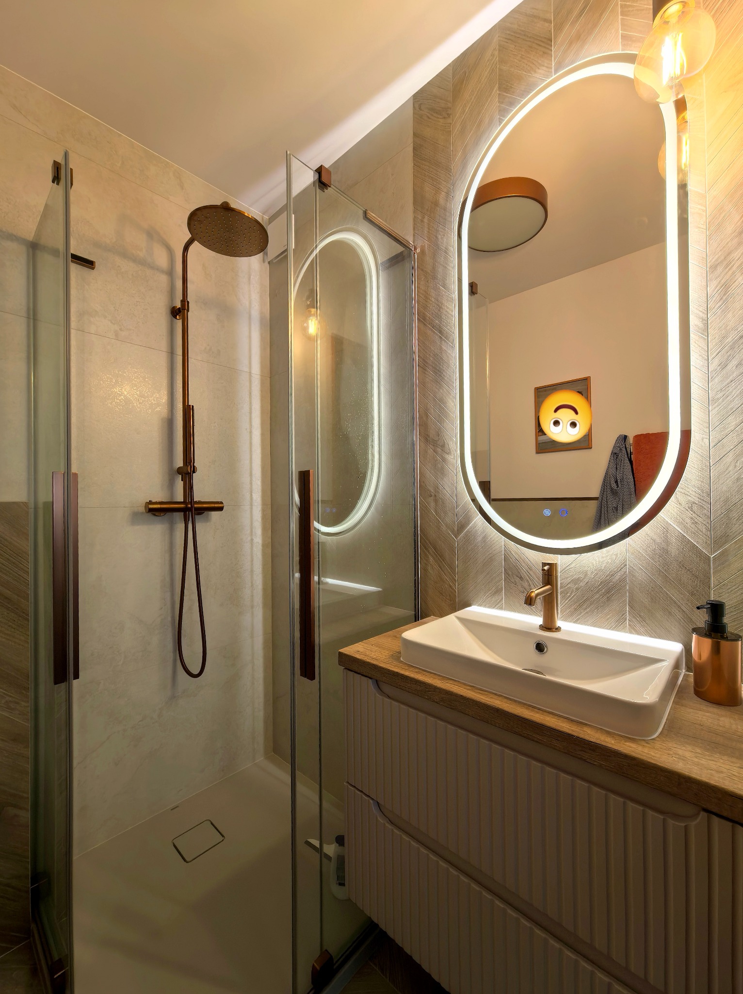 Nowoczesna łazienka z kabiną prysznicową typu walk-in, umywalką nablatową i podświetlanym lustrem w kształcie łuku. Armatura w kolorze miedzi.