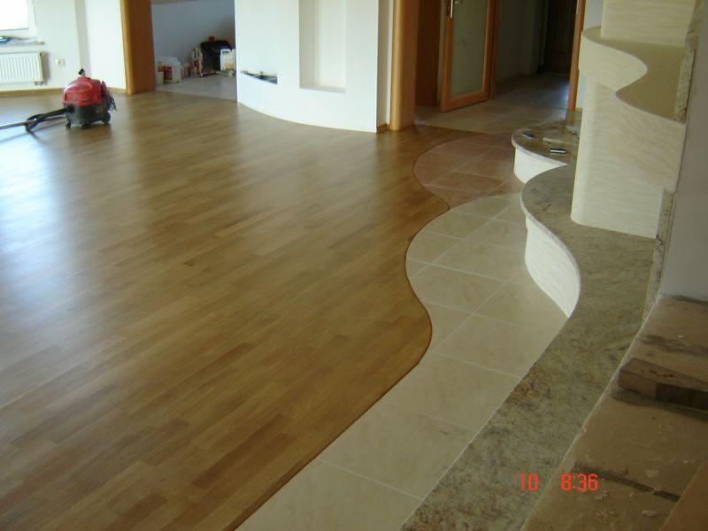 Połączenie paneli podłogowych z mozaiką ceramiczną w łukowatym przejściu, widoczny odkurzacz na parkiecie w tle.