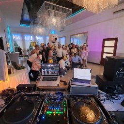Alternatywne Brzmienie - AB Sound & Music Studio - DJ prezentuje sprzęt (dwa laptopy, mikser, gramofony) przed grupą w maskach w sali z oświetleniem imprezowym. W tle dekoracja z misiem.