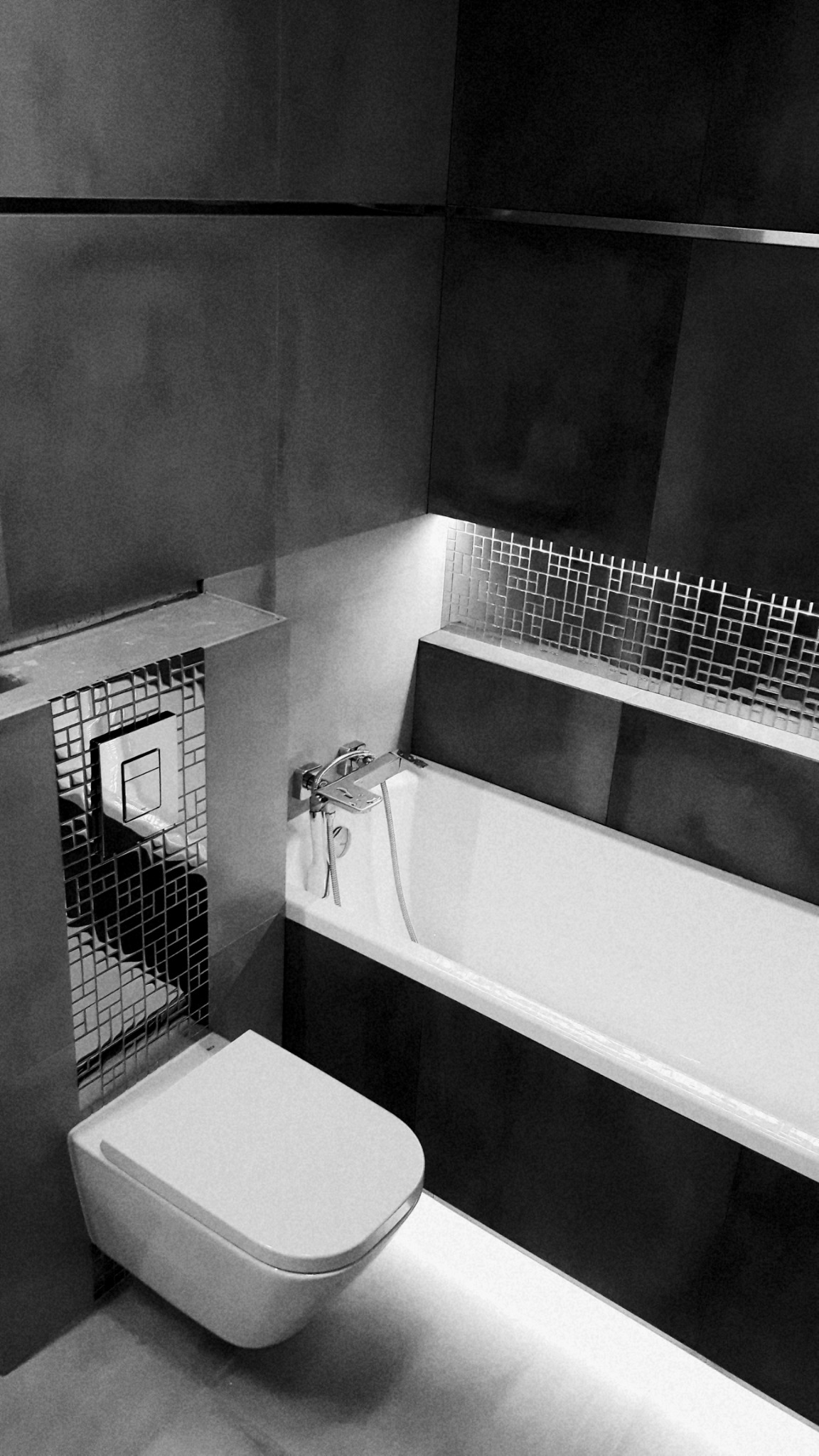 Czarno-biała fotografia wykończonej łazienki z wiszącą toaletą i wanną, podkreślona mozaiką i subtelnym oświetleniem LED.