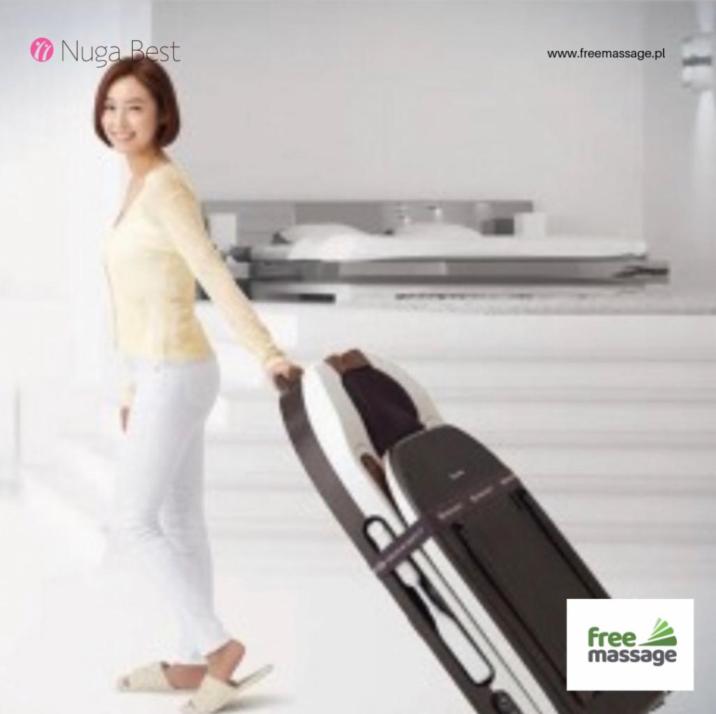 Kobieta prezentuje rozłożone łóżko masujące Nuga Best w jasnym wnętrzu, widoczne logo firmy.
