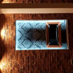 Ściana z cegły z dekoracyjnym, podświetlanym panelem z wzorem i drewnianą wnęką, oświetlona lampami punktowymi, widoczny odkurzacz. Nietypowe wykończenie wnętrza.