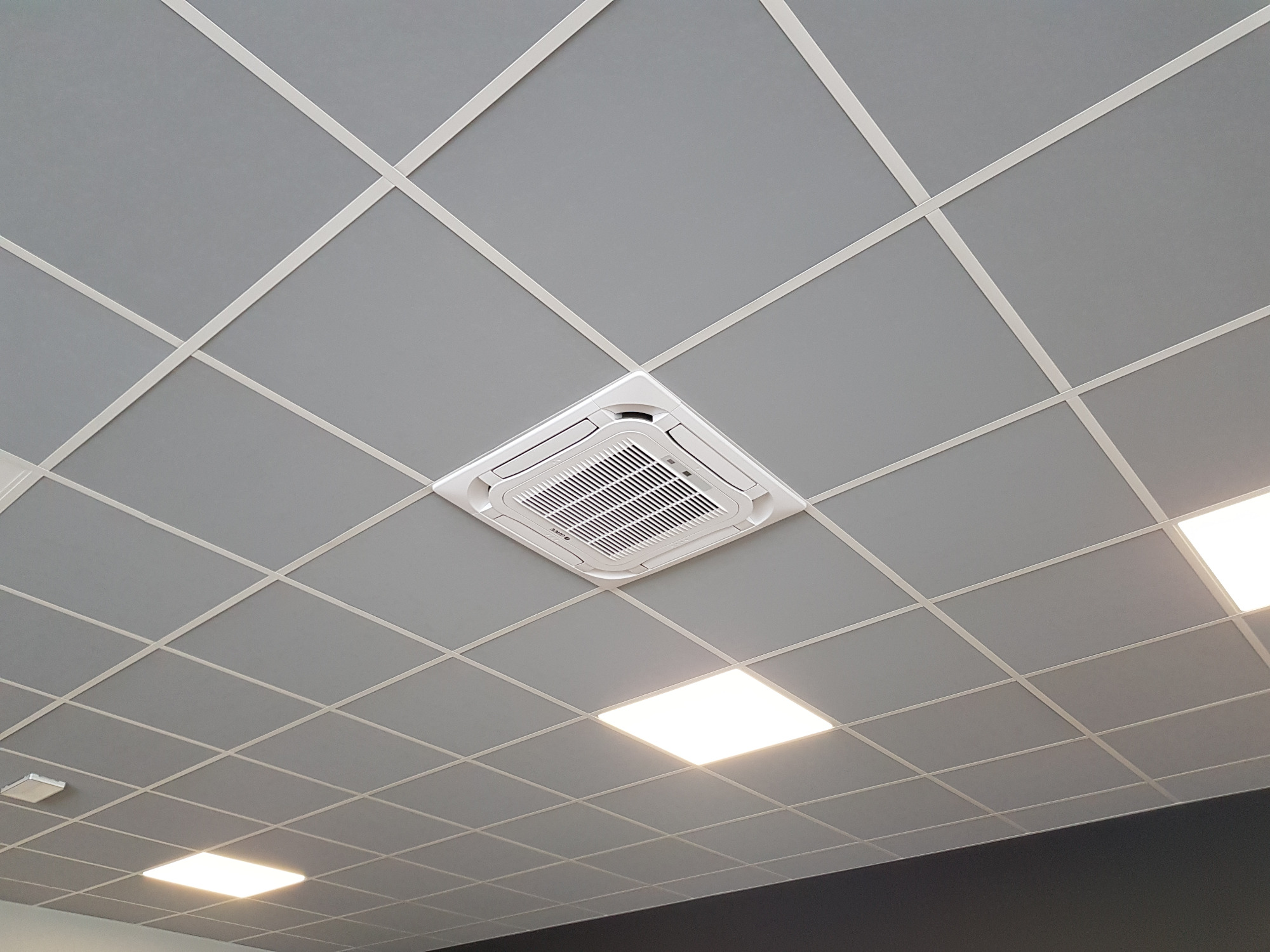 Kasetonowy sufit z wbudowaną centralną jednostką klimatyzacji kasetonowej, widoczne kratki wentylacyjne i oświetlenie LED.