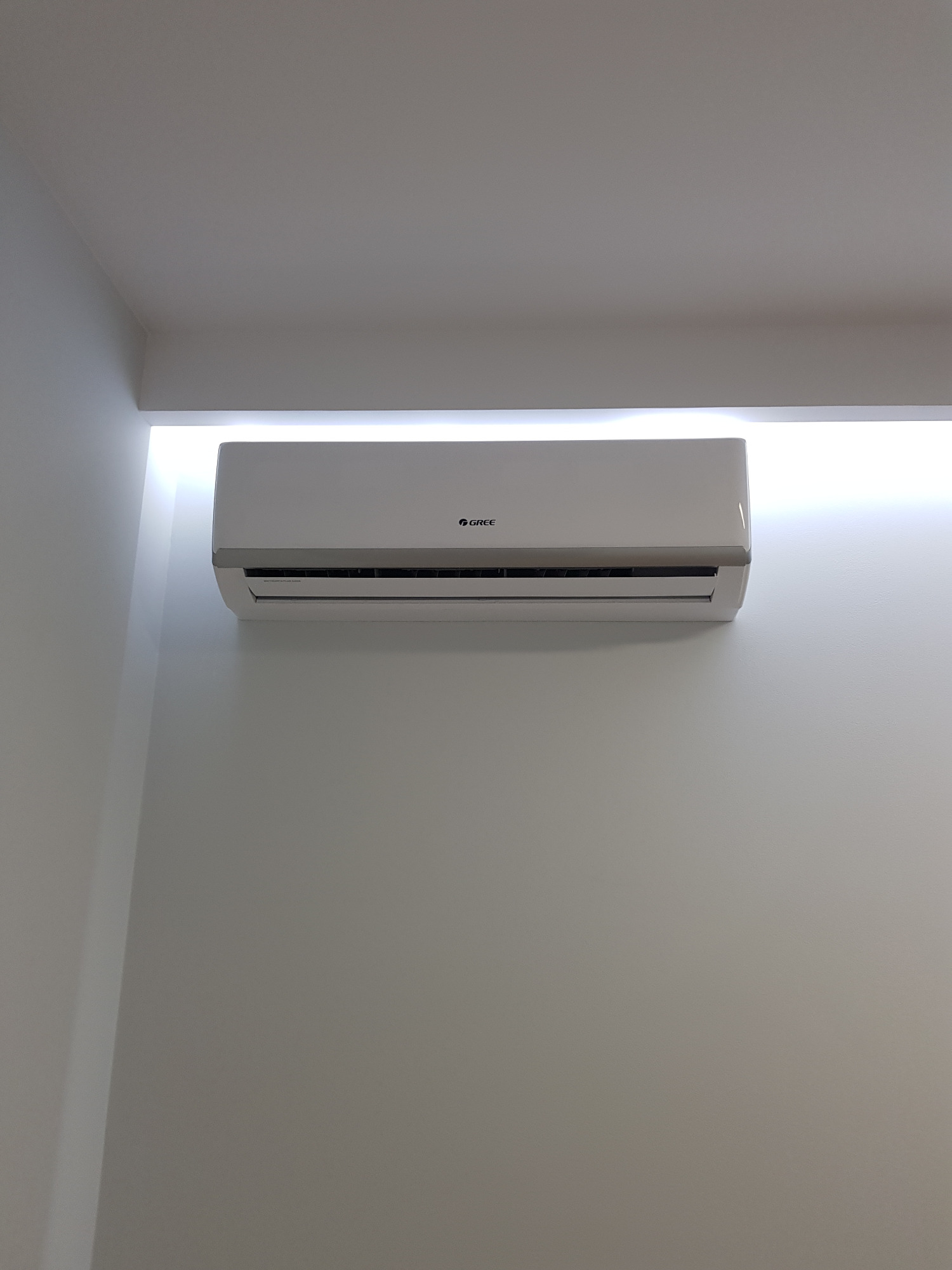 Biały klimatyzator marki Gree zamontowany na białej ścianie pod sufitem z wbudowanym oświetleniem LED.
