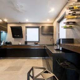 Nowoczesna kuchnia z czarnymi szafkami, drewnianymi akcentami i szarą płytką, oświetlona designerską lampą sufitową i wyposażona w metalowy regał na wino.