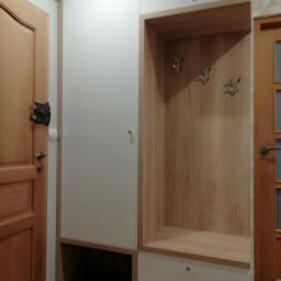 GUD meble - Biało-drewniana szafa wnękowa z otwartą przestrzenią na wieszaki i dolną szafką, widoczna obok drewnianych drzwi wejściowych.