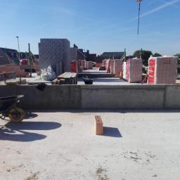 P.W.KOWAL Daniel Kowalski - Wznoszenie ścian z bloczków na fundamencie domu, widoczny dźwig budowlany w tle i pojedynczy bloczek na pierwszym planie.