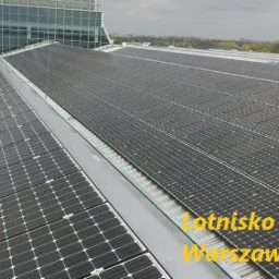 Rozległa instalacja paneli słonecznych na dachu budynku lotniska Chopina w Warszawie, widok z góry na panele, w tle zabudowa miejska.