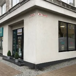 Zewnętrzny widok narożnej kliniki z szyldem i oknami z reklamami, adres na rogu budynku.