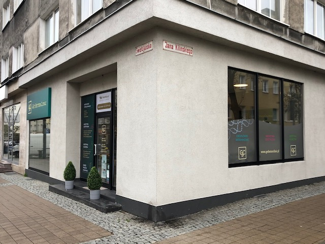 Zewnętrzny widok narożnej kliniki z szyldem i oknami z reklamami, adres na rogu budynku.