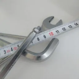 Klucze imbusowe, klucz płaski i miarka zwinięta na białym tle, ułożone pod kątem.