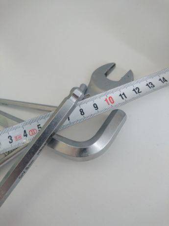 Klucze imbusowe, klucz płaski i miarka zwinięta na białym tle, ułożone pod kątem.