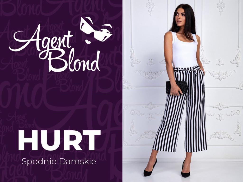 Modelka prezentuje szerokie spodnie w czarno-białe paski z wiązaniem w pasie, biały top i czarne szpilki na tle ściany ze sztukaterią, obok logo firmy odzieżowej.