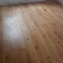 Nowo ułożone panele podłogowe w jasnym odcieniu drewna, widok z niskiej perspektywy na fragment pokoju z grzejnikiem pod oknem.