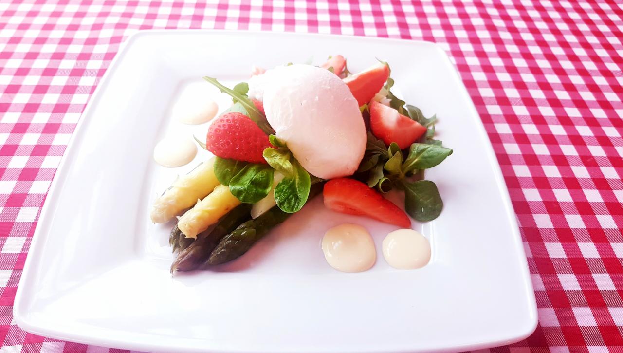 Wykwintna sałatka z białych i zielonych szparagów, truskawek, rukoli i kremowego sera na białym kwadratowym talerzu, ozdobiona kroplami sosu, prezentowana przez firmę z Plewisk na tle...