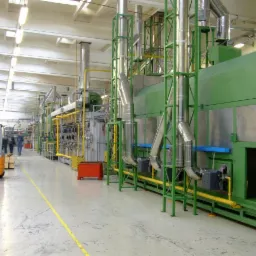 Wnętrze hali produkcyjnej z linią technologiczną do obróbki metali, z widocznym wózkiem widłowym STILL i pracownikami w tle.