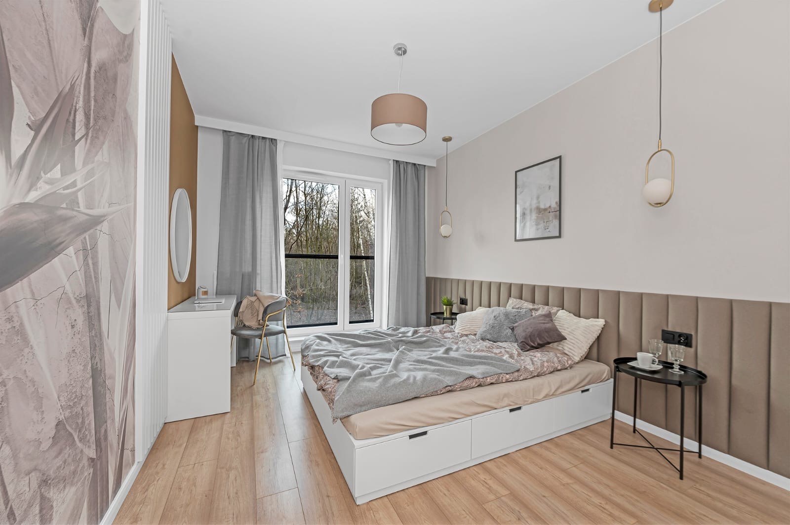 Jasna sypialnia z łóżkiem z szufladami, tapicerowanym wezgłowiem, stolikami nocnymi, lampami wiszącymi i dużym oknem z widokiem na las.