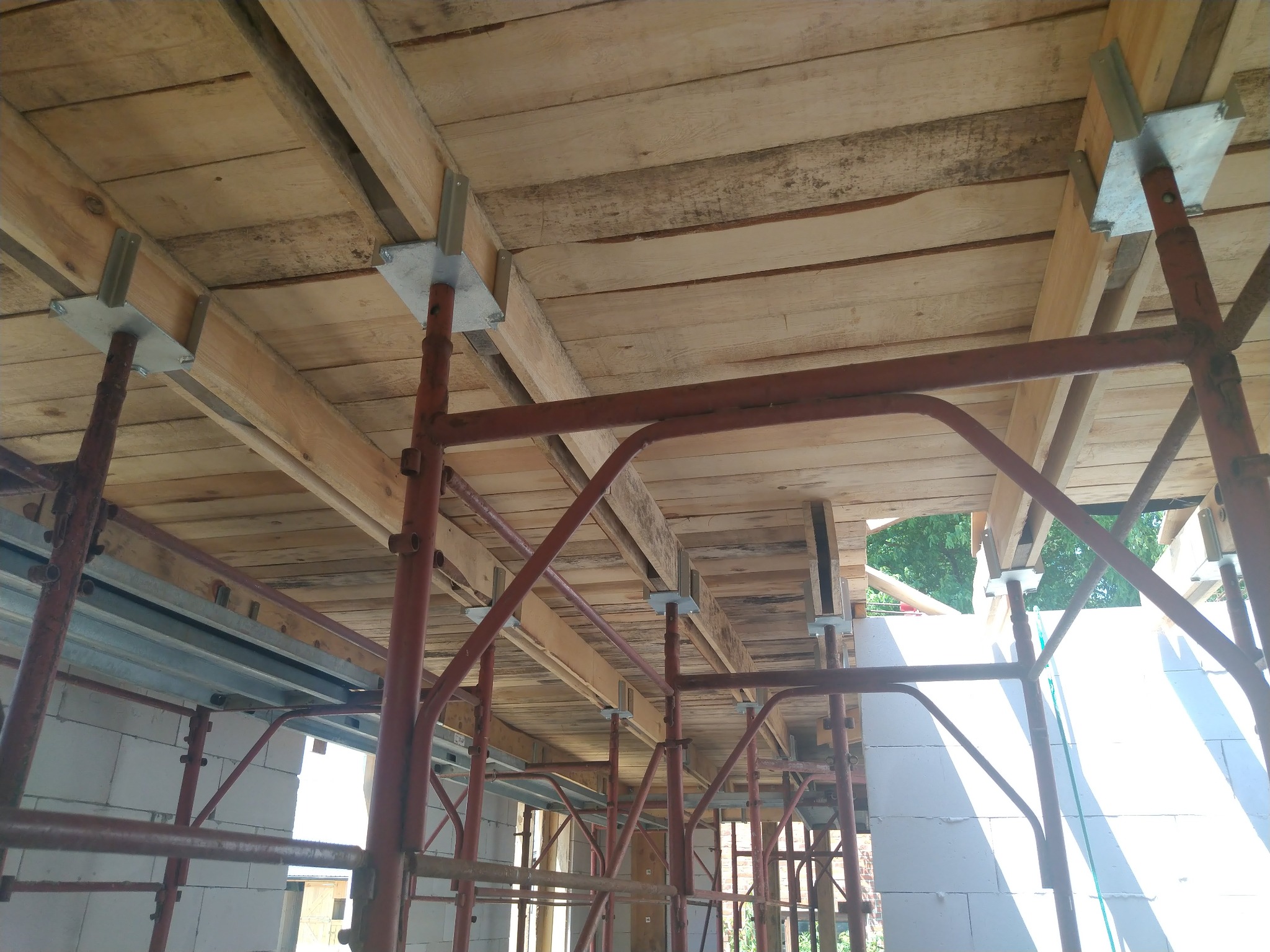 Wnętrze budowanego domu z białych bloczków, widoczny drewniany strop podparty metalowymi stemplami szalunkowymi w kolorze czerwonym.