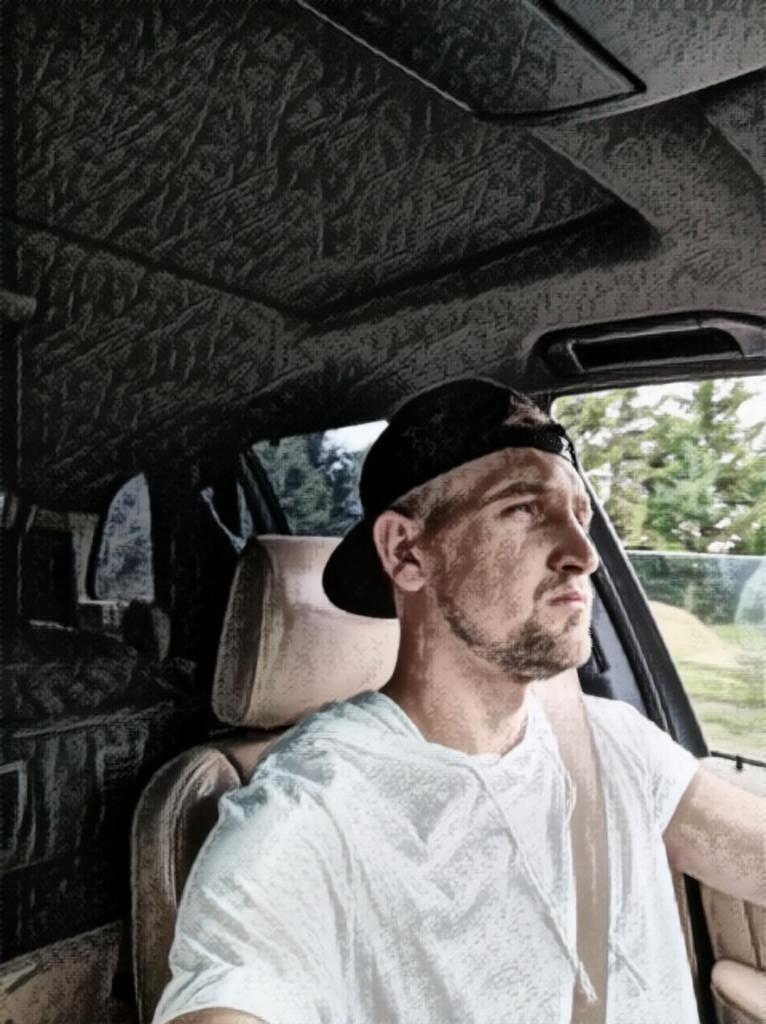 Mężczyzna w czapce bejsbolówce siedzi w samochodzie, patrzy w prawo. Widoczne wnętrze auta i drzewa za oknem. Stylizacja zdjęcia przypomina szkic.