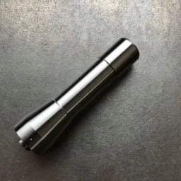 Metalowy, cylindryczny element z widocznymi śladami obróbki skrawaniem, leżący na szorstkiej, metalowej powierzchni.